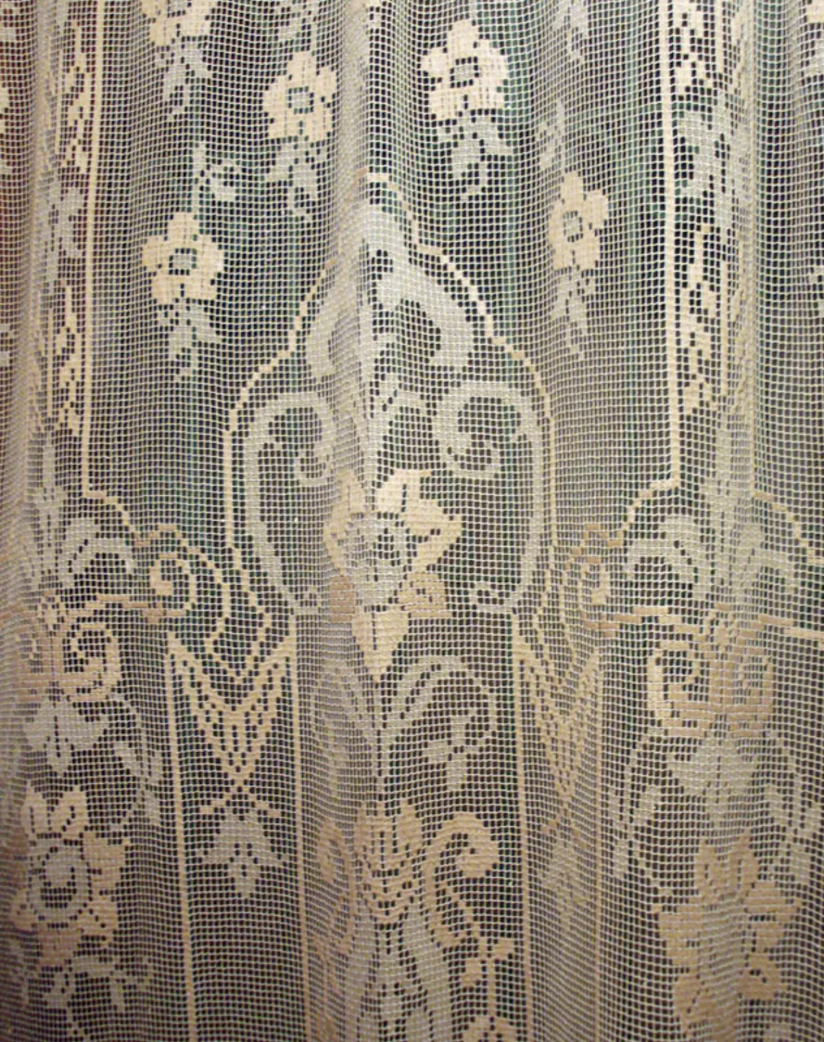 A real filet crochet curtain with large floral motifs built from solid cells against open mesh