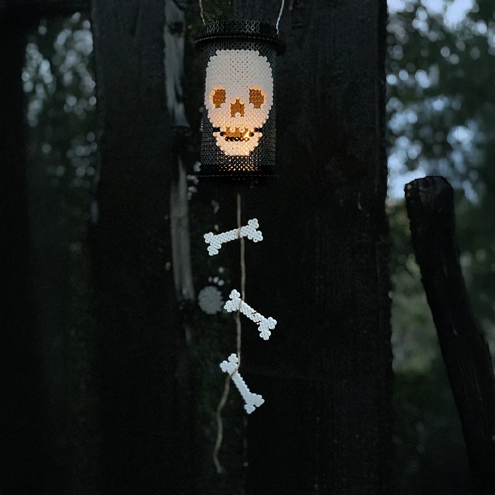 A real Hama skeleton lantern glows above a vertical garland of fused bead bones in an outdoor Halloween display